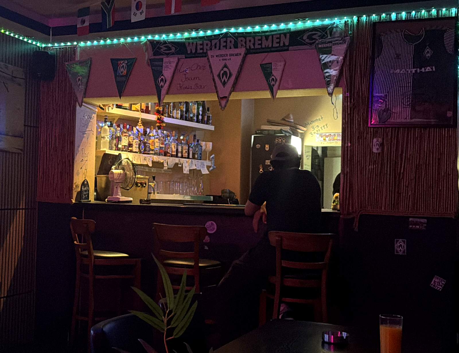 Die Theke der Koala Bar: Werder-Wimpel, türkises Licht, Barhocker und das beleuchtete Flaschenregal
